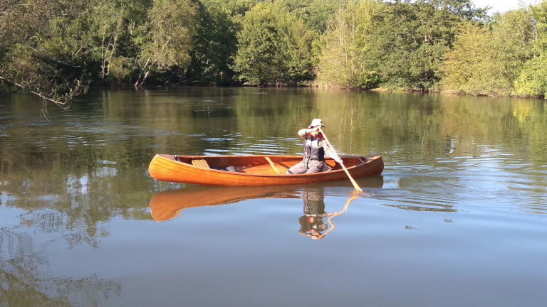 Paddler in a wooden open touring canoe paddling on a river